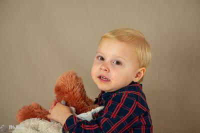 Un enfant souriant en t-shirt blanc pose avec une main sous le menton sur un fond clair.