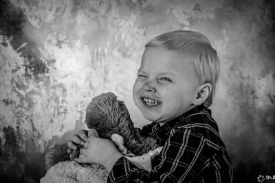 Un enfant souriant en t-shirt blanc pose avec une main sous le menton sur un fond clair.