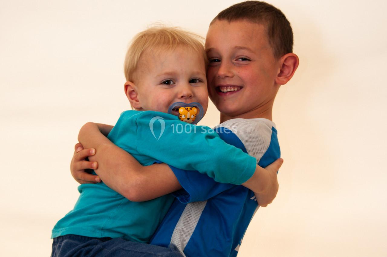 Deux jeunes enfants souriants, l'un portant l'autre dans ses bras, sur un fond clair.
