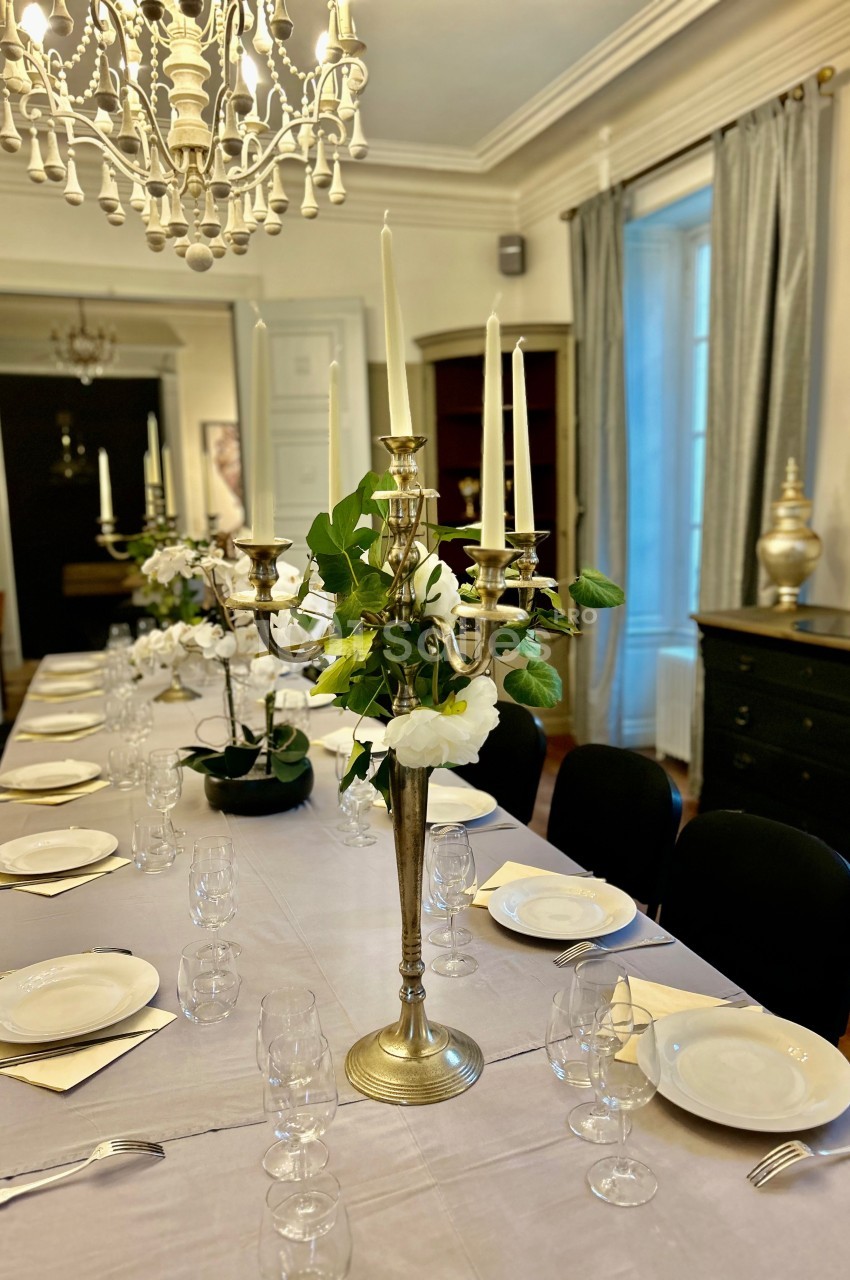 Table élégamment dressée avec chandeliers dorés, vaisselle blanche et décoration florale dans une salle lumineuse.