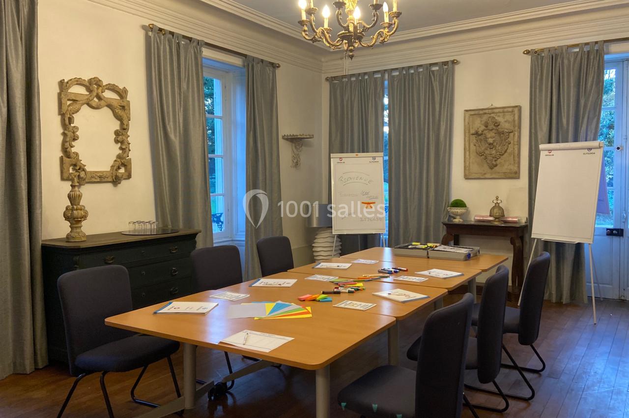 Salle de réunion lumineuse avec table en bois, chaises, paperboards, fournitures de bureau et décoration classique.
