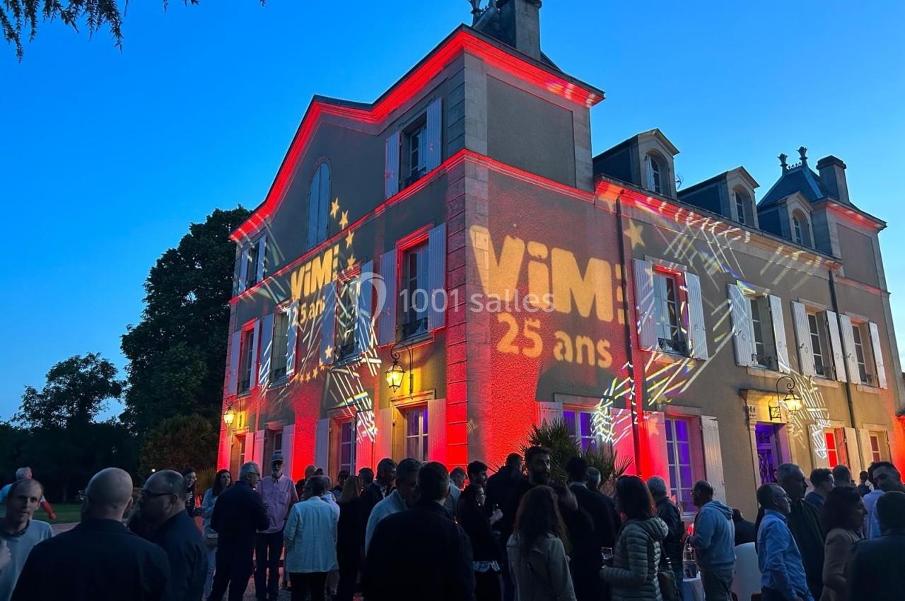 Façade d'un bâtiment illuminée par des projections lumineuses, avec une foule rassemblée devant au crépuscule.