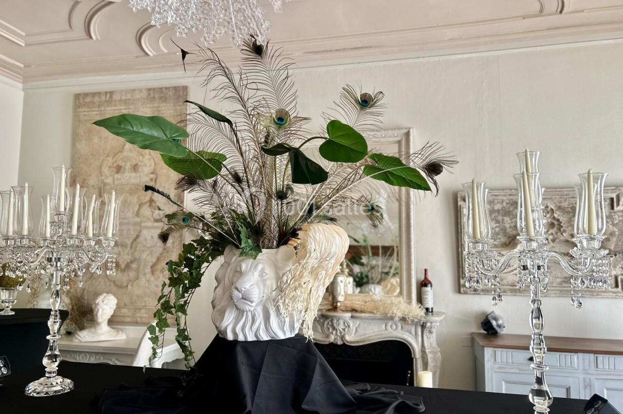 Vase en forme de tête de lion avec des feuilles tropicales et des plumes de paon, posé sur une table élégante.