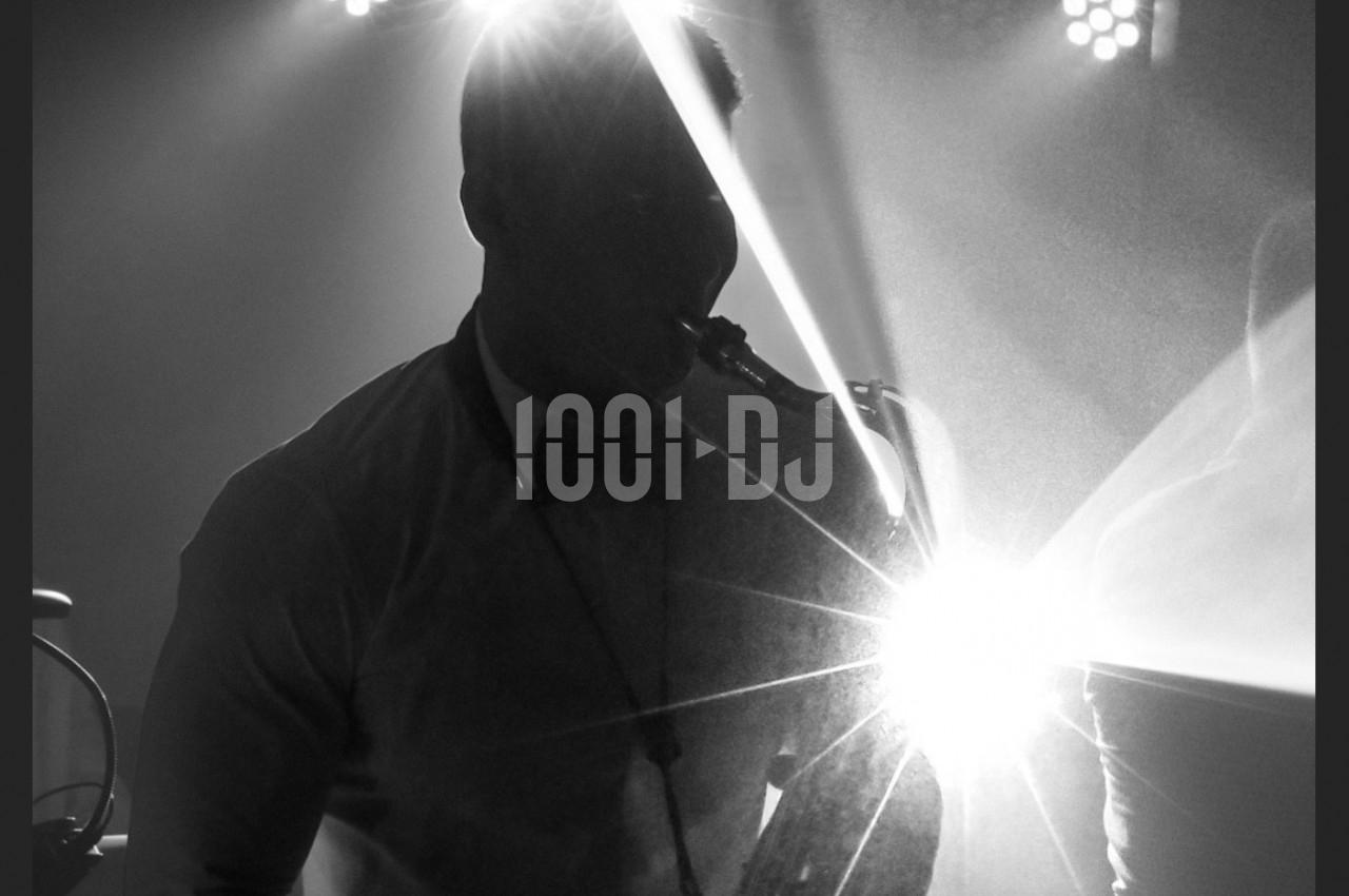 Un musicien joue du saxophone sur une scène éclairée par des projecteurs, créant des effets lumineux.