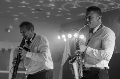 Miniature DJ Carcès (Var) - Dj Sax à Tout Coeur #6 Un homme en costume bleu tient un saxophone dans un intérieur lumineux avec de grandes fenêtres.