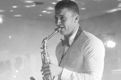 Miniature DJ Carcès (Var) - Dj Sax à Tout Coeur #7 Un homme en costume bleu tient un saxophone dans un intérieur lumineux avec de grandes fenêtres.