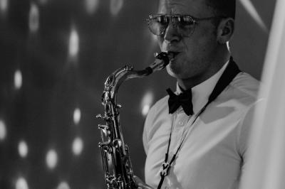 Miniature DJ Carcès (Var) - Dj Sax à Tout Coeur #10 Un homme en costume bleu tient un saxophone dans un intérieur lumineux avec de grandes fenêtres.