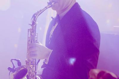 Miniature DJ Carcès (Var) - Dj Sax à Tout Coeur #15 Un homme en costume bleu tient un saxophone dans un intérieur lumineux avec de grandes fenêtres.