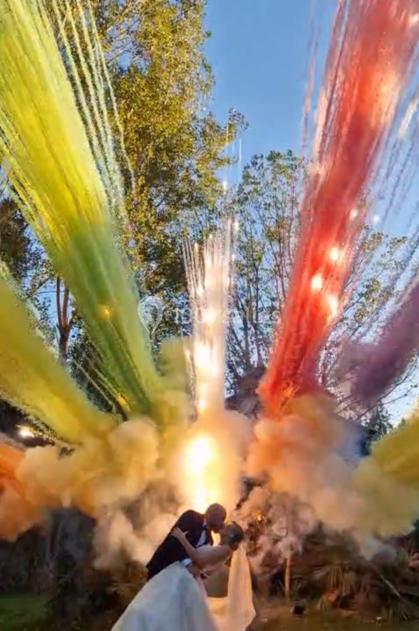 Un couple s'embrasse dans un jardin, entouré de feux d'artifice colorés illuminant le ciel au coucher du soleil.