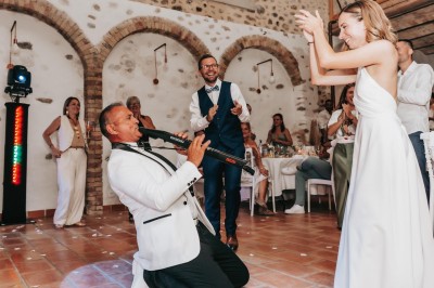 Un homme en costume bleu tient un saxophone sous une pergola décorée de fleurs blanches.