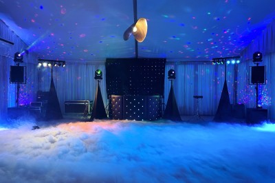 Un homme en costume bleu tient un saxophone sous une pergola décorée de fleurs blanches.