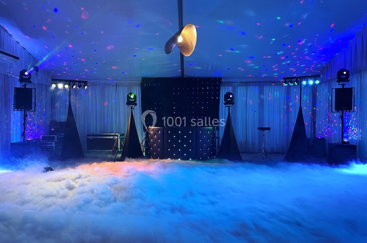 Salle de réception avec éclairage coloré, piste de danse entourée de fumée et équipement de sonorisation.