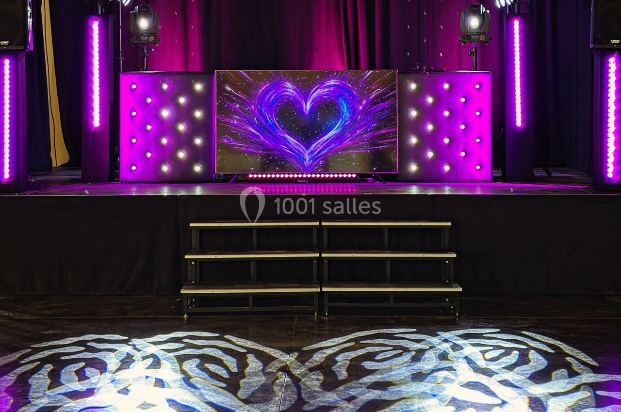 Scène décorée avec des lumières violettes, un écran affichant un cœur lumineux et des motifs projetés au sol.