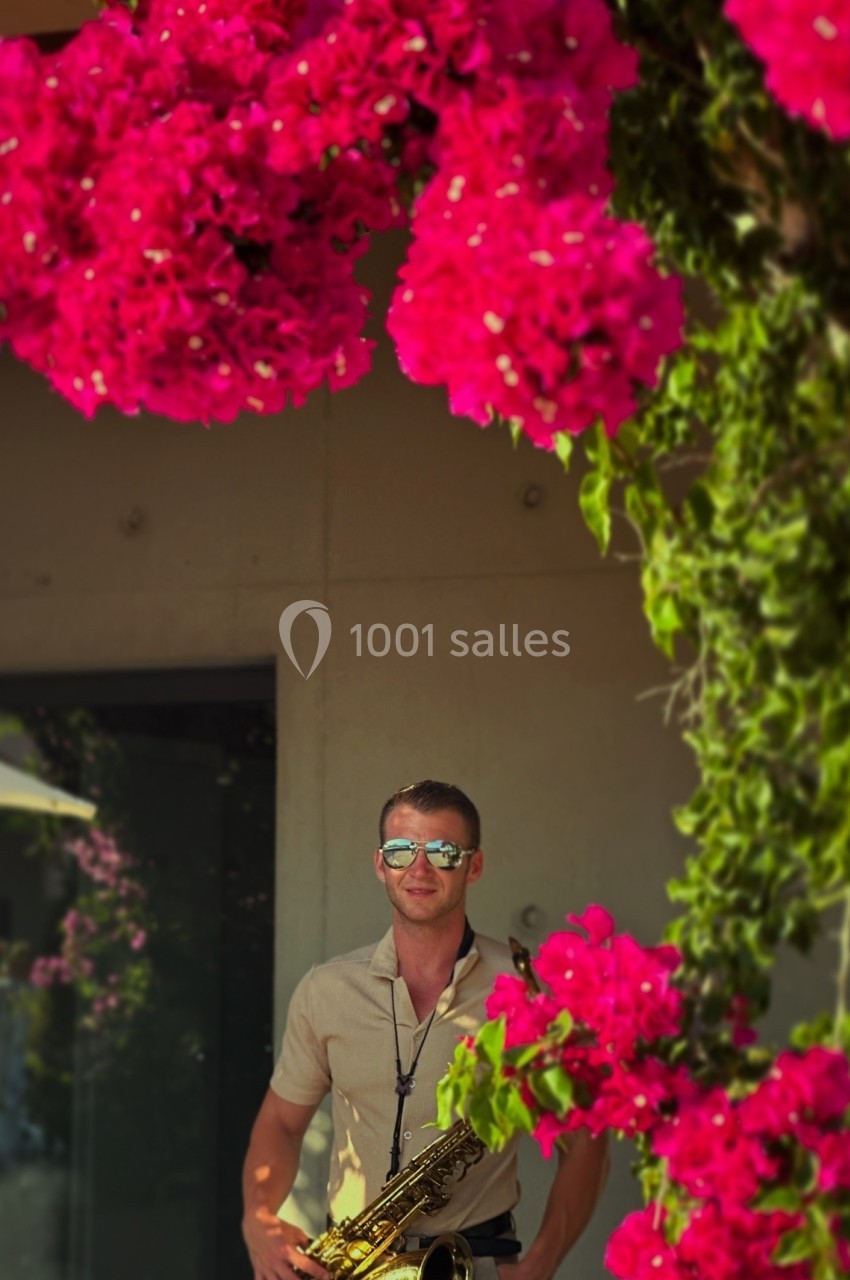 Un homme jouant du saxophone devant un mur décoré de bougainvilliers roses.