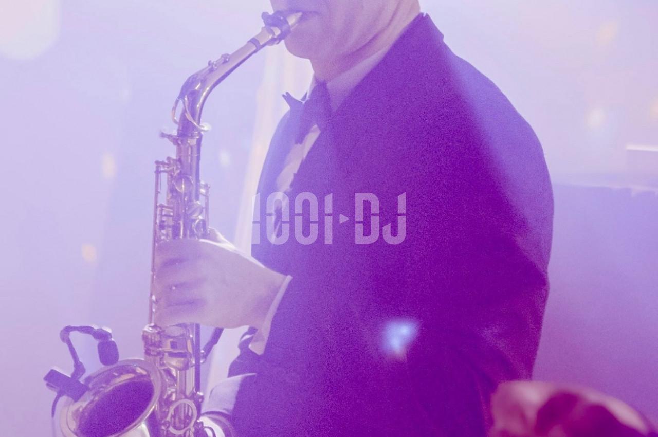 Un musicien en smoking joue du saxophone dans une ambiance lumineuse tamisée.