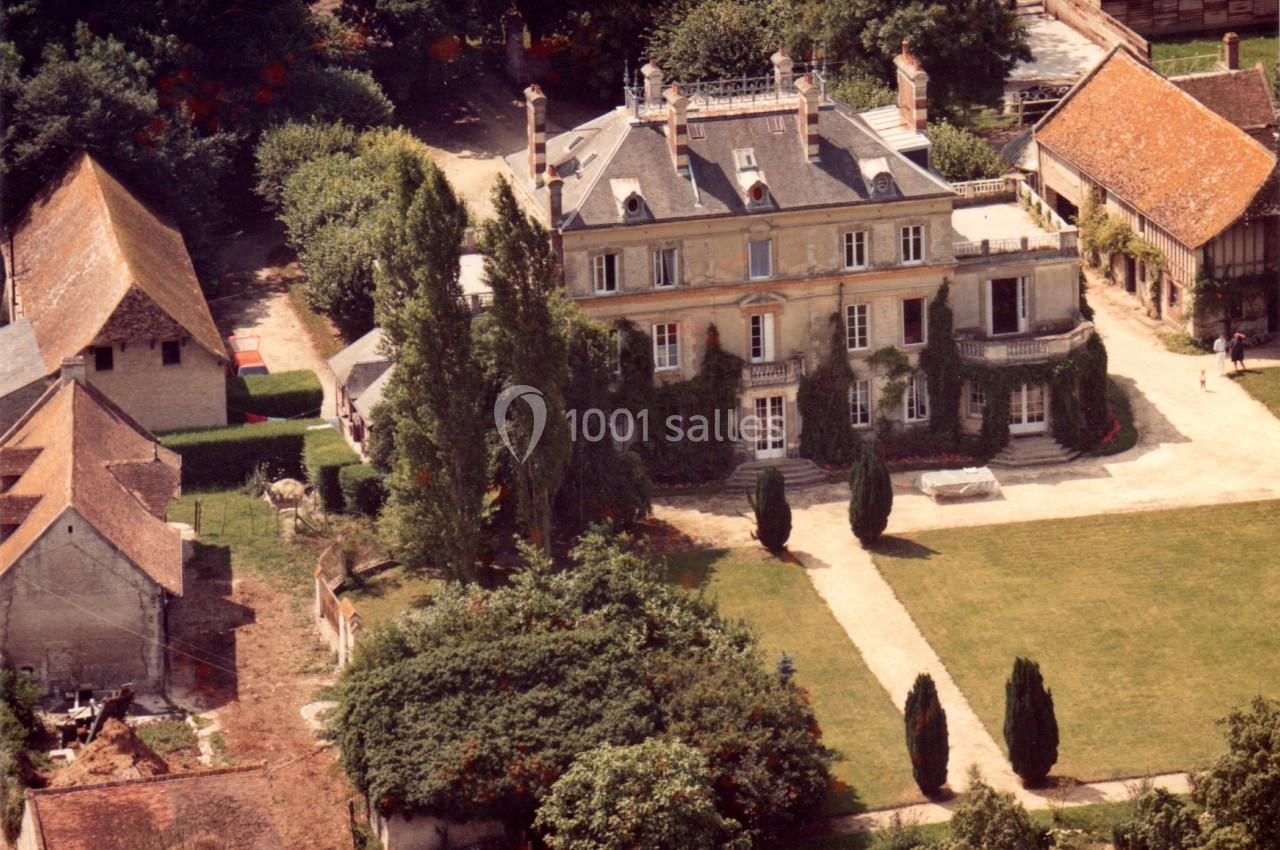 Vue aérienne d'un manoir entouré de jardins, d'arbres et de bâtiments annexes dans un cadre rural.
