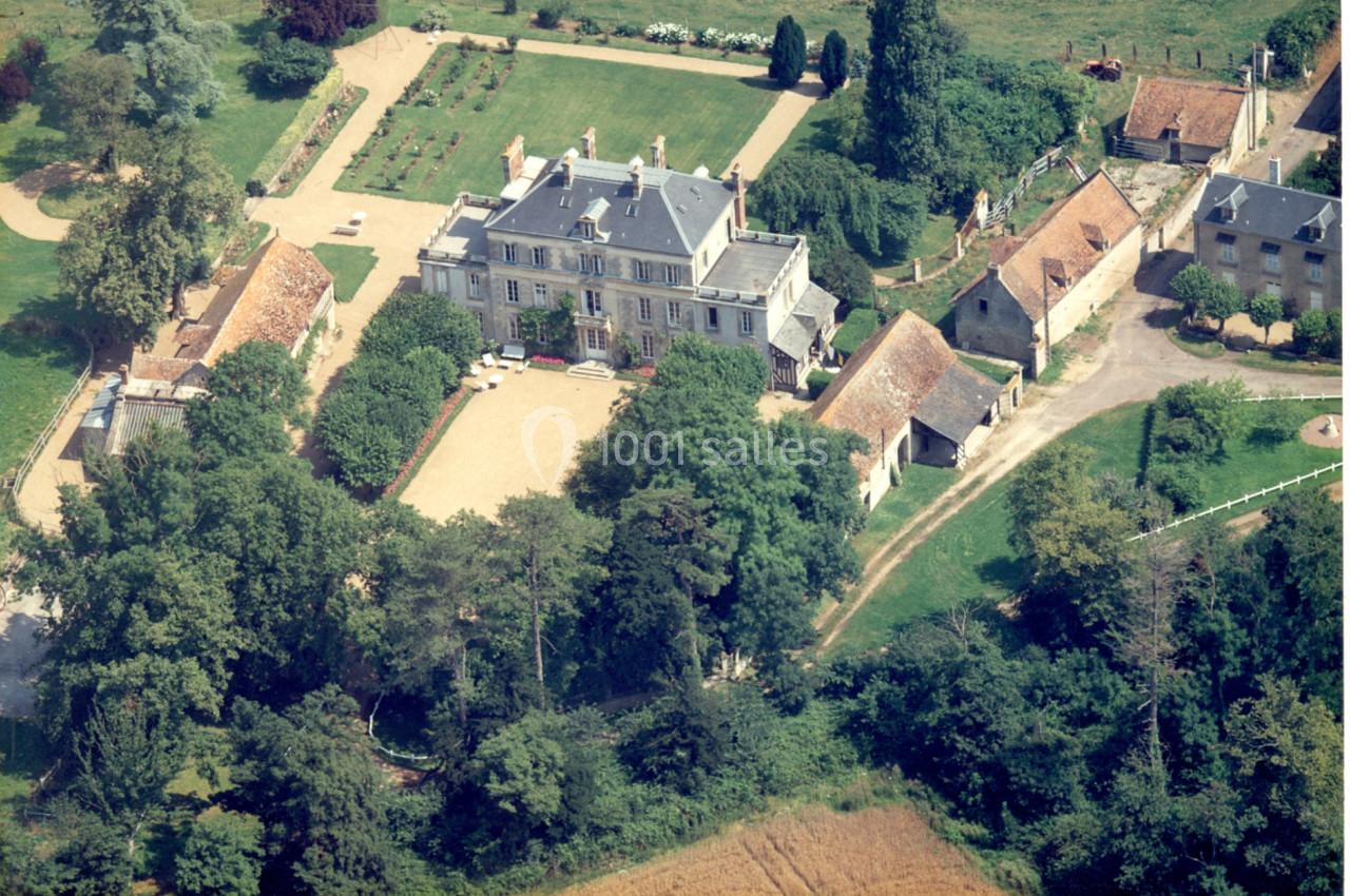 Vue aérienne d'un domaine avec un manoir central, des bâtiments annexes, un jardin et des espaces boisés environnants.