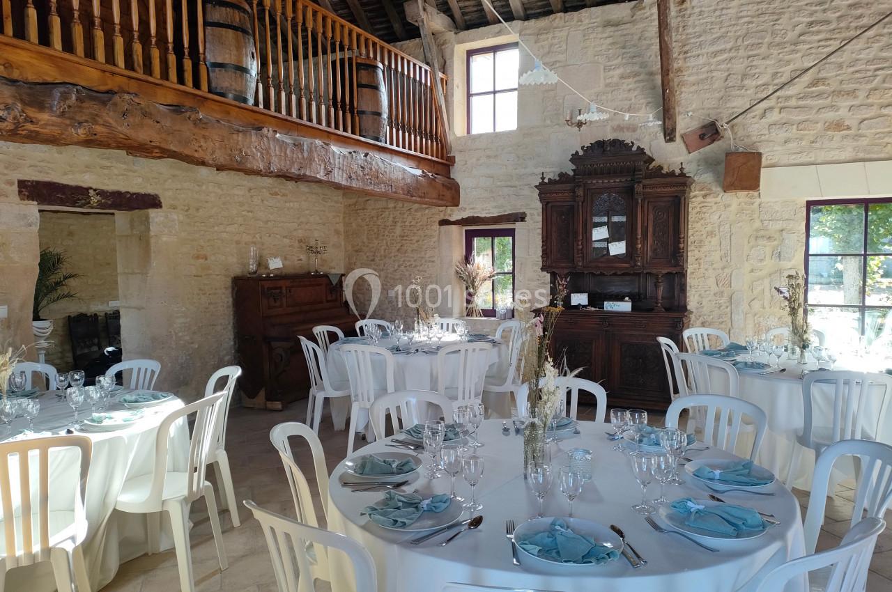 Salle de réception rustique avec murs en pierre, tables dressées avec nappes blanches et décoration bleue.