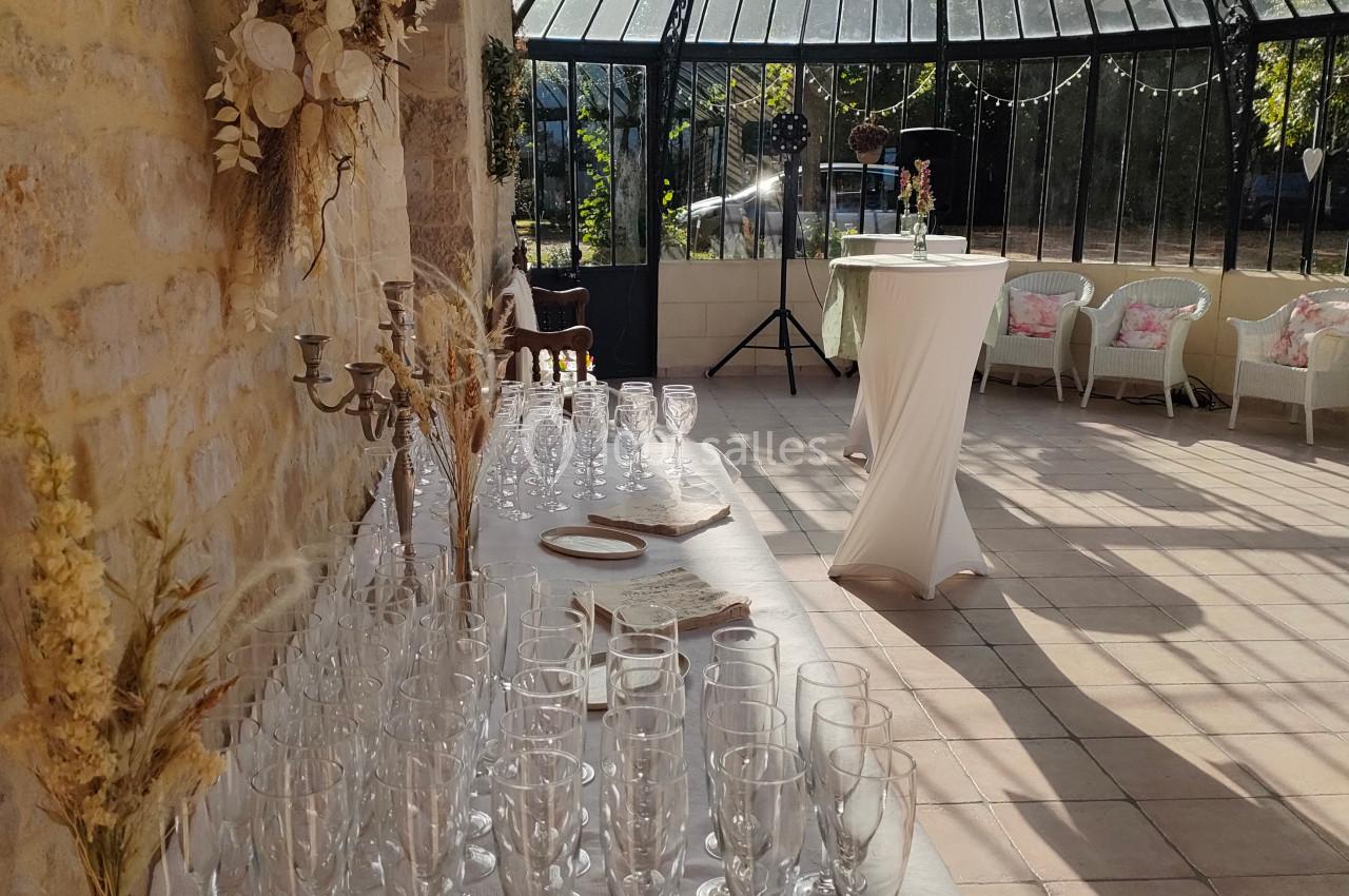 Table dressée avec des verres à pied dans une salle lumineuse avec verrière, décorée de fleurs séchées et mobilier élégant.