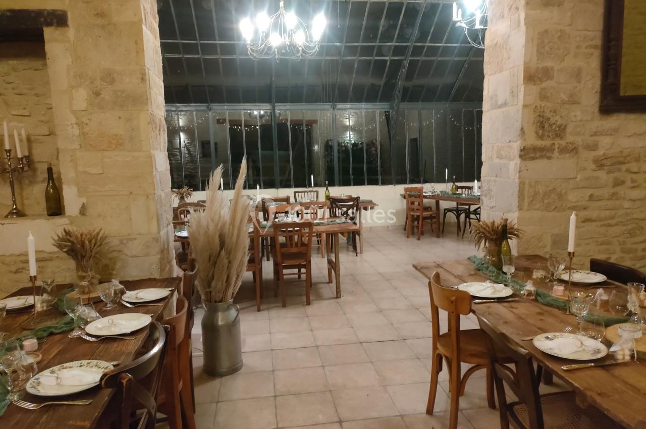 Salle de réception avec tables en bois dressées, décor champêtre et grandes baies vitrées en arrière-plan.