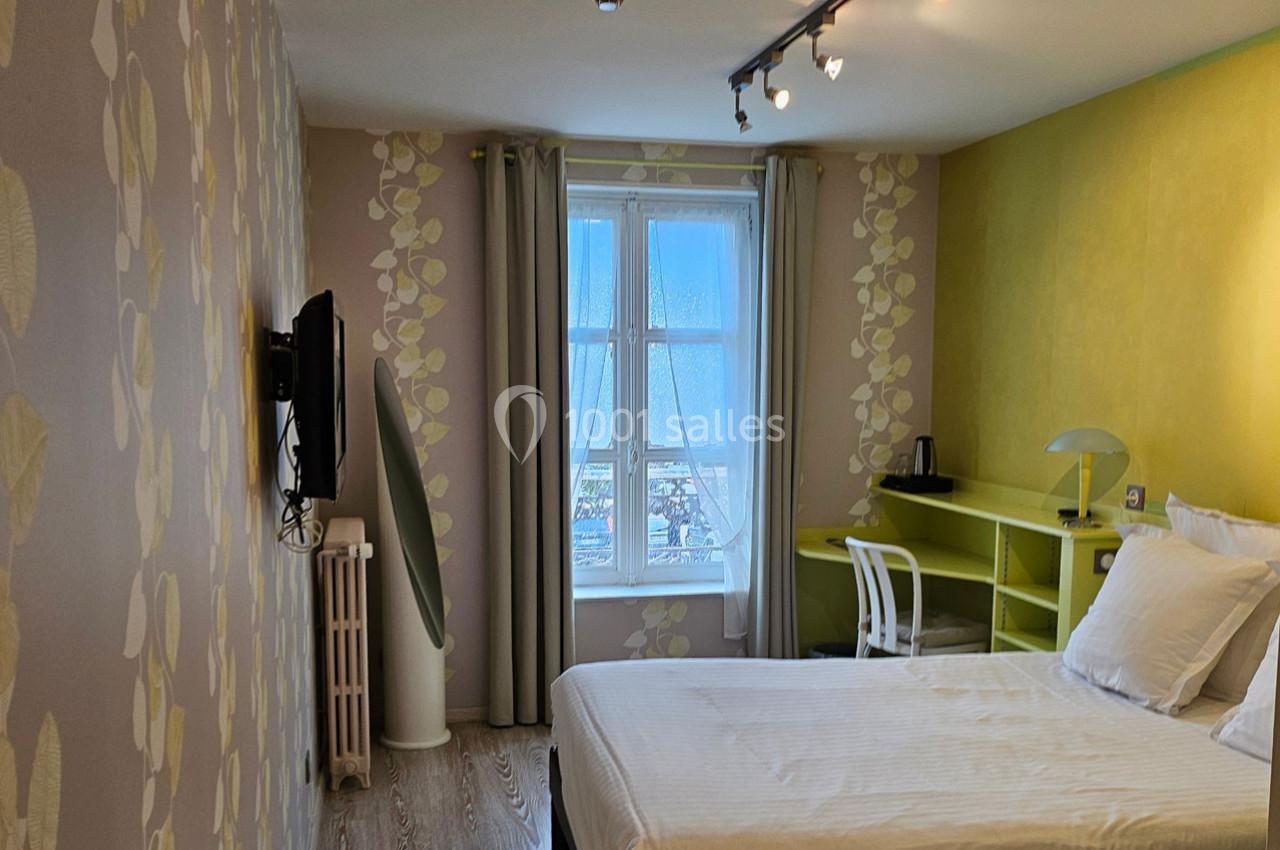 Chambre lumineuse avec lit double, bureau, télévision murale et grande fenêtre donnant sur une vue extérieure.