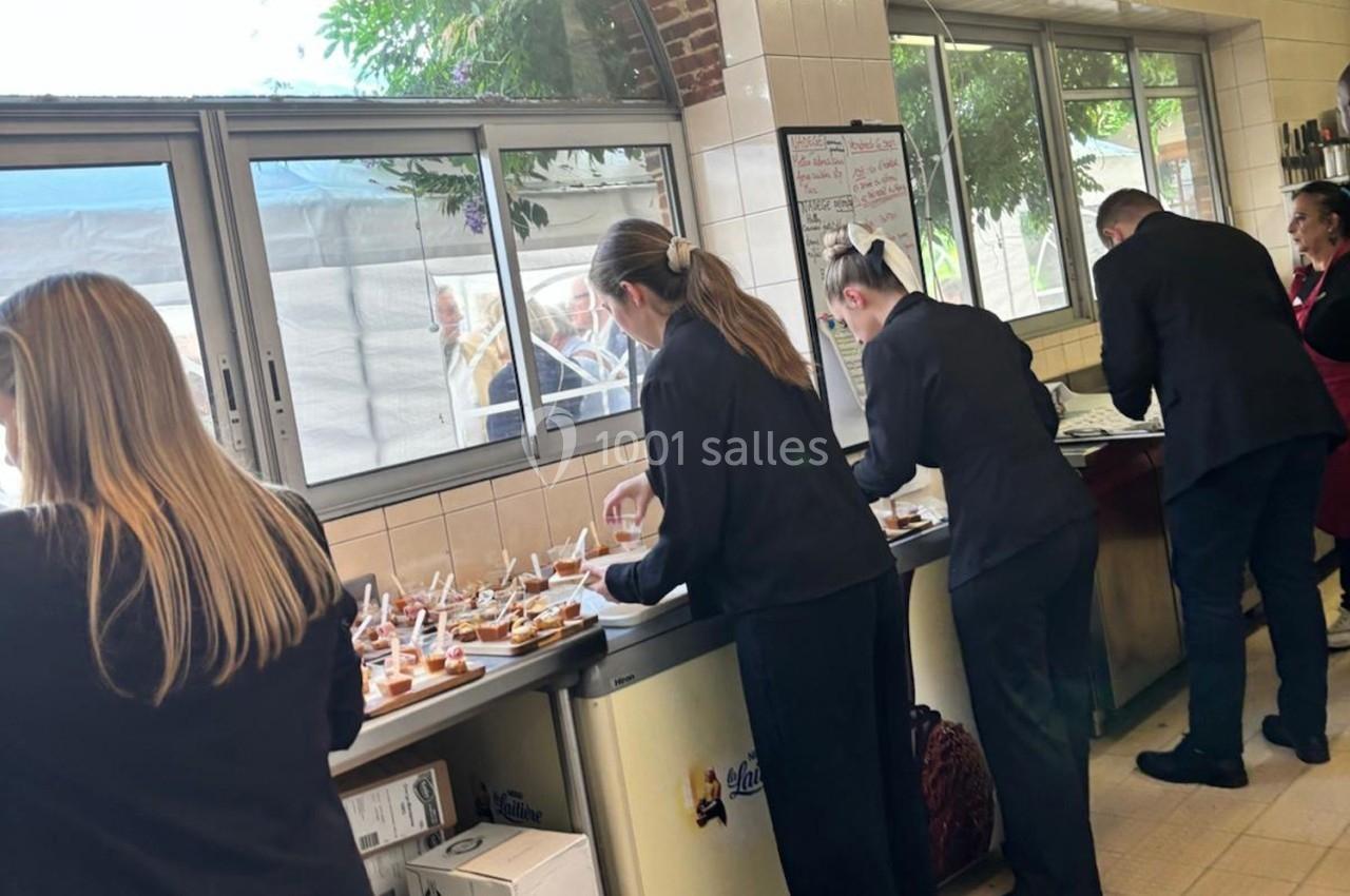 Des serveurs en tenue professionnelle préparent des plateaux de bouchées dans une cuisine lumineuse.