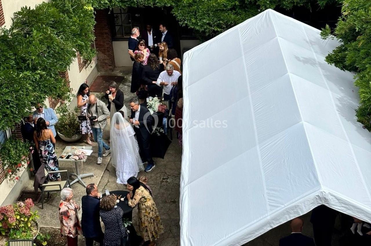 Groupe de personnes rassemblées dans une cour extérieure sous un chapiteau blanc, lors d'un événement festif.