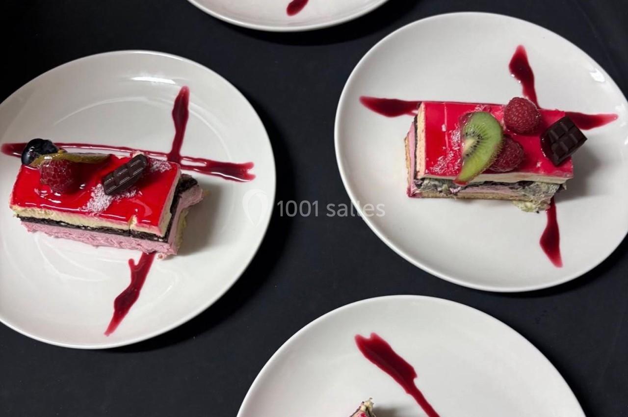 Tranches de gâteau à la mousse fruitée et glaçage rouge, décorées de fruits et servies sur des assiettes blanches.