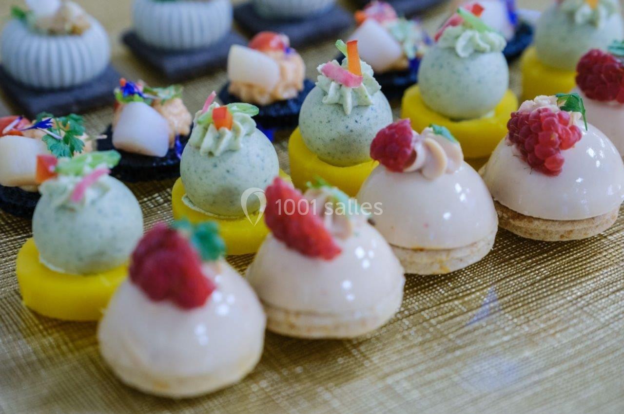 Assortiment de petits desserts raffinés sur une table dorée, comprenant fruits, crèmes et décorations colorées.