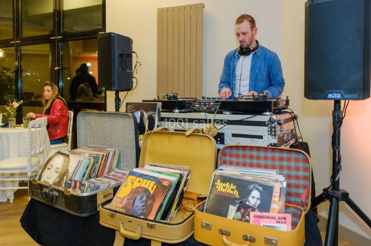 Un DJ mixe de la musique sur une table de mixage, entouré de valises remplies de disques vinyles.