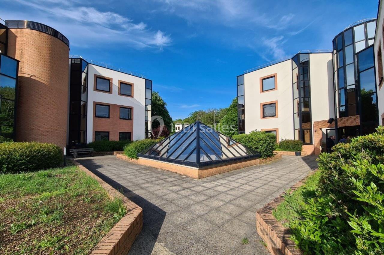 Cour intérieure avec une verrière pyramidale entourée de bâtiments modernes en briques et grandes fenêtres vitrées.