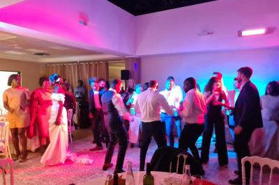 Salle décorée avec des ballons roses, éclairage violet, deux personnes marchant au centre, tables hautes et chaises…