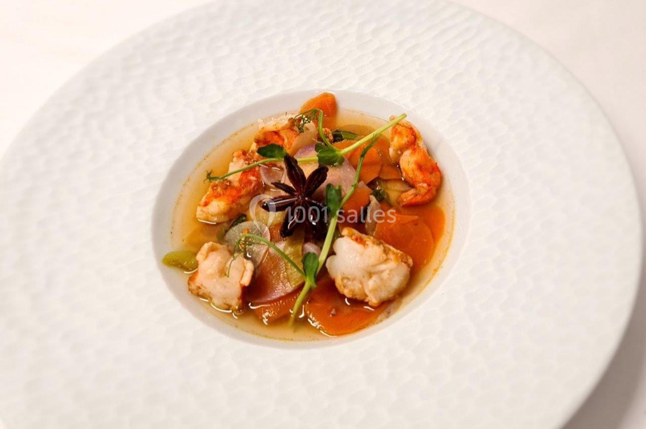 Assiette de soupe raffinée avec gambas, légumes colorés et étoile de badiane en décoration.