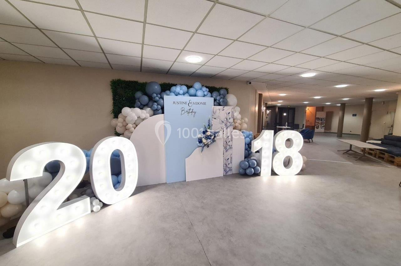 Décoration événementielle avec chiffres lumineux ’2018’, mur de ballons et panneau personnalisé dans une salle éclairée.