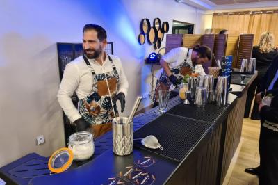Salle décorée avec des ballons roses, éclairage violet, deux personnes marchant au centre, tables hautes et chaises…
