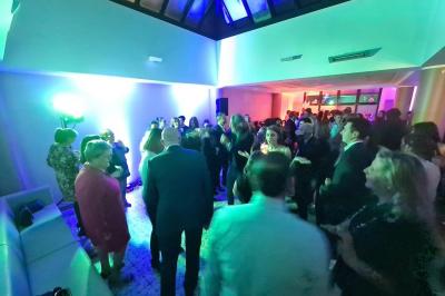Salle décorée avec des ballons roses, éclairage violet, deux personnes marchant au centre, tables hautes et chaises…