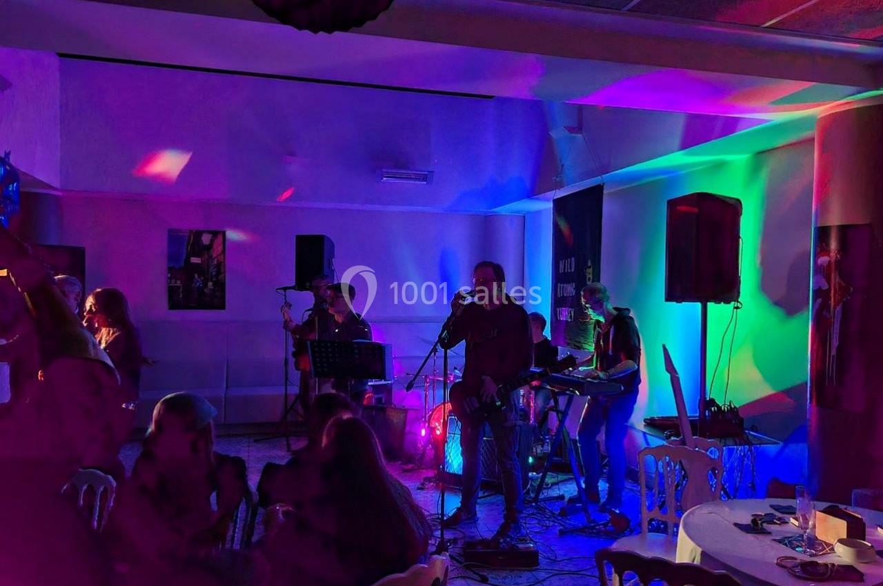 Groupe de musiciens jouant sur une scène éclairée par des lumières colorées dans une salle avec des spectateurs assis.