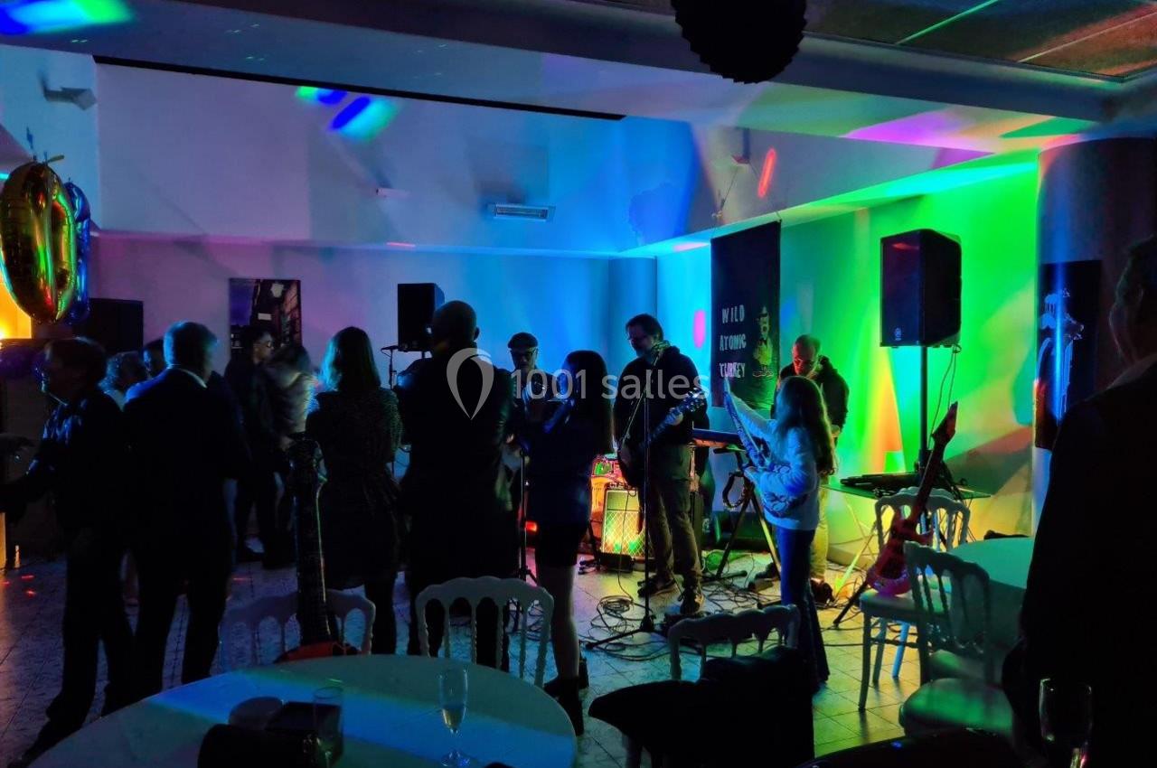 Groupe de musiciens jouant sur scène dans une salle éclairée par des lumières colorées, entourés de spectateurs debout.