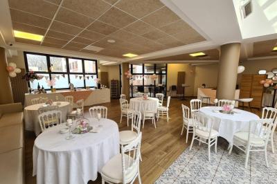 Salle décorée avec des ballons roses, éclairage violet, deux personnes marchant au centre, tables hautes et chaises…