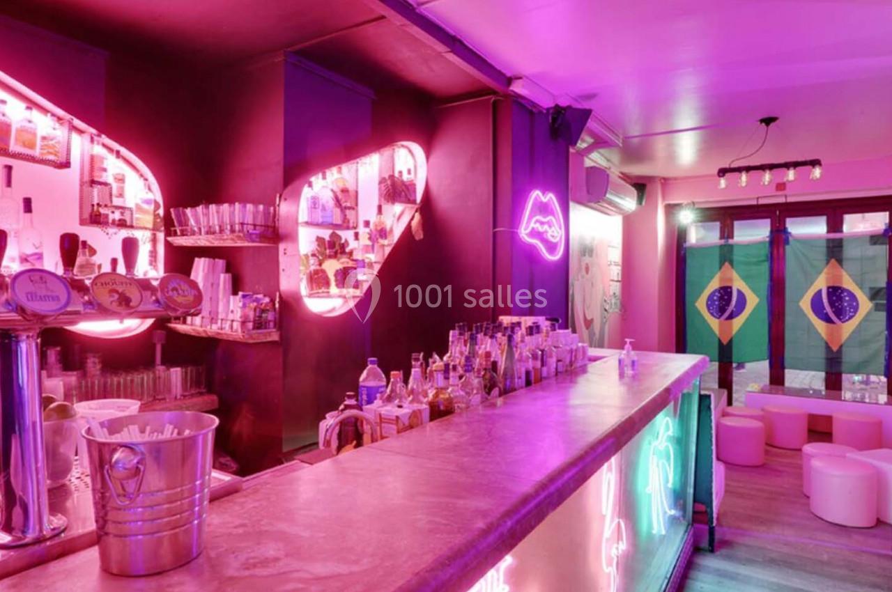 Bar éclairé par des néons roses, avec comptoir en premier plan et drapeaux brésiliens accrochés au fond.