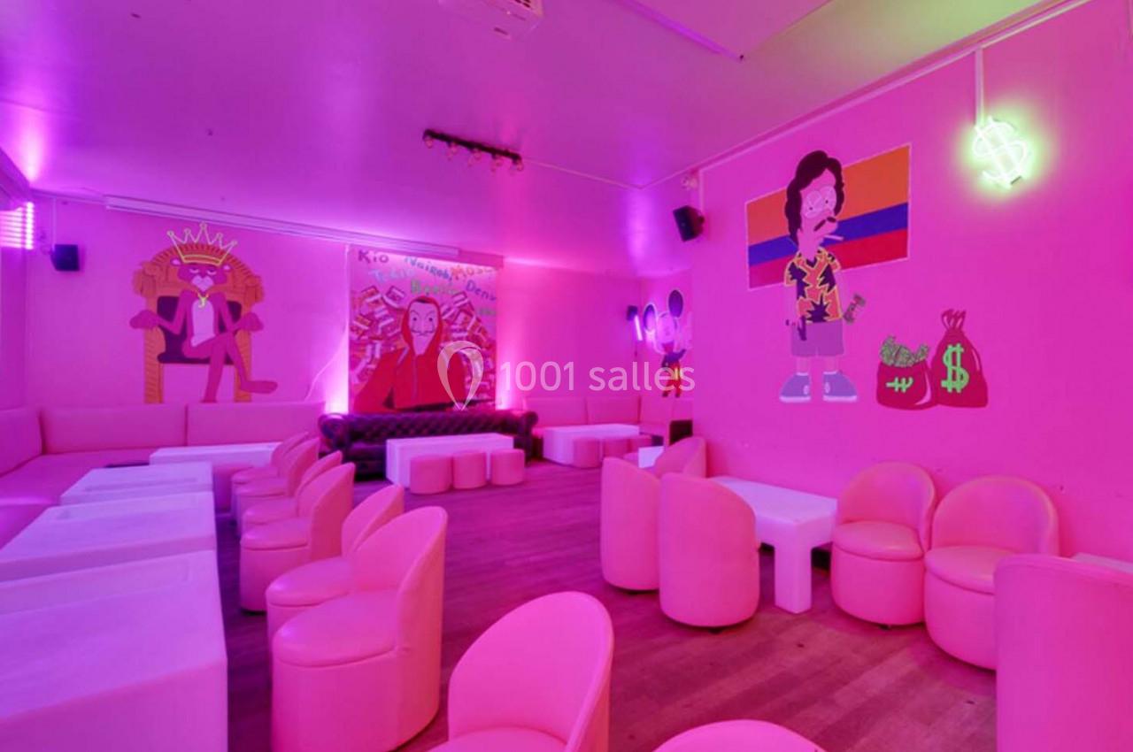 Salle lumineuse avec des murs roses, des illustrations colorées, des néons et des sièges modernes disposés autour de tables…