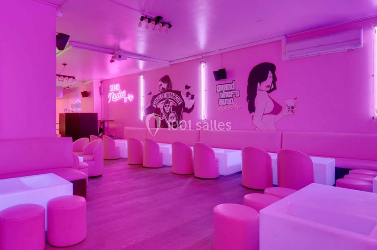 Salle de bar aux murs roses avec banquettes blanches, tabourets assortis et néons décoratifs.