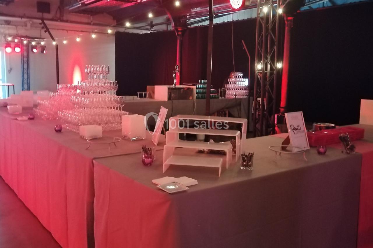 Tables de buffet avec verrerie empilée, présentoirs blancs et décorations lumineuses dans une salle éclairée en rouge.