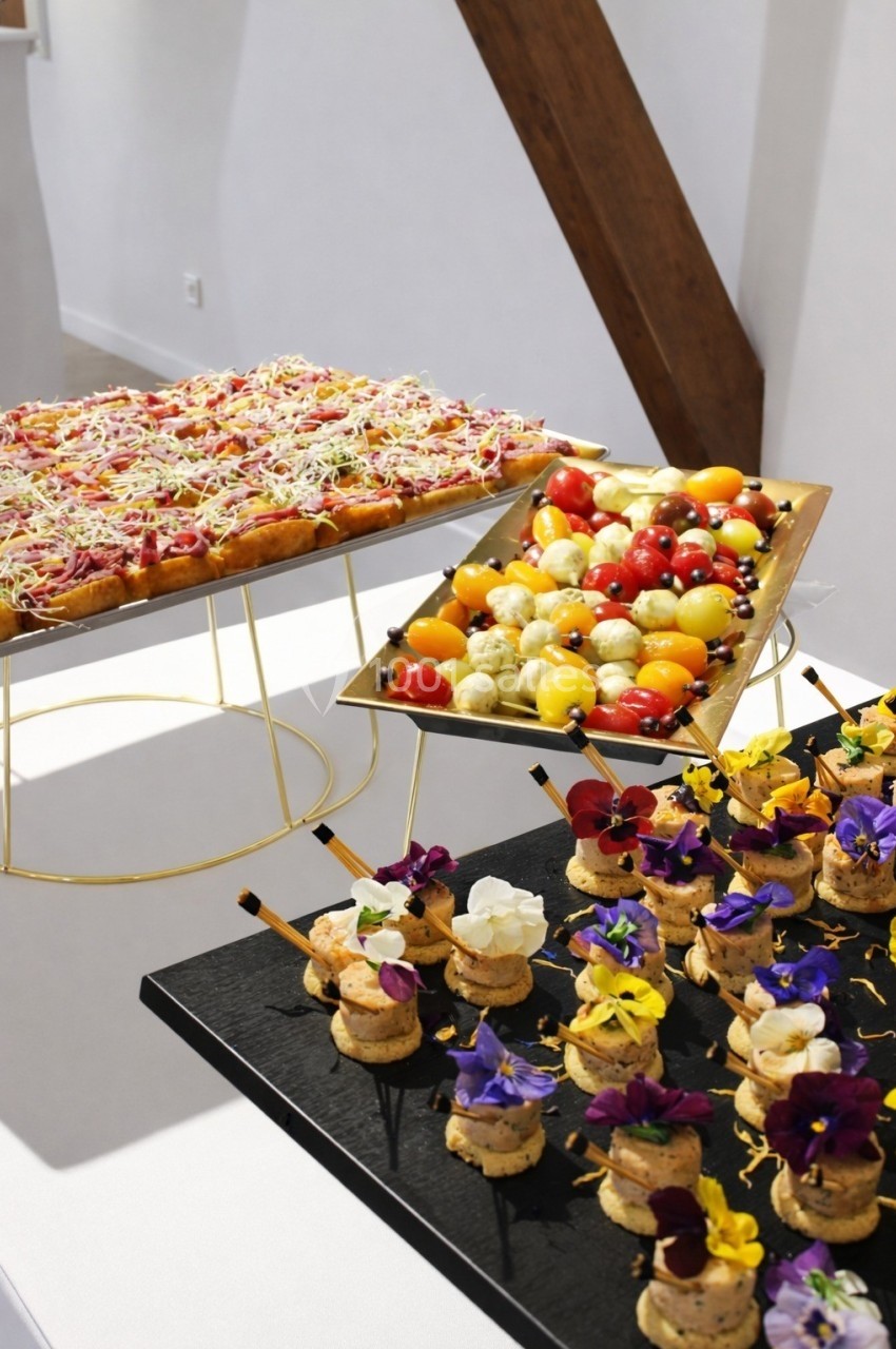 Plateaux de bouchées apéritives variées, incluant canapés fleuris, brochettes de tomates et tarte colorée.
