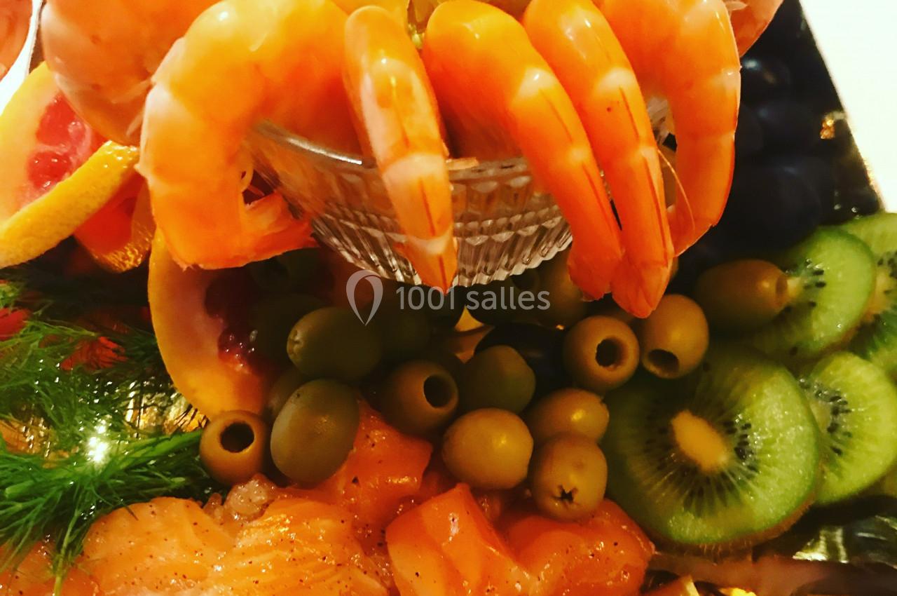 Assortiment de fruits de mer avec crevettes, saumon, olives, kiwis et tranches d'agrumes disposés sur un plateau.