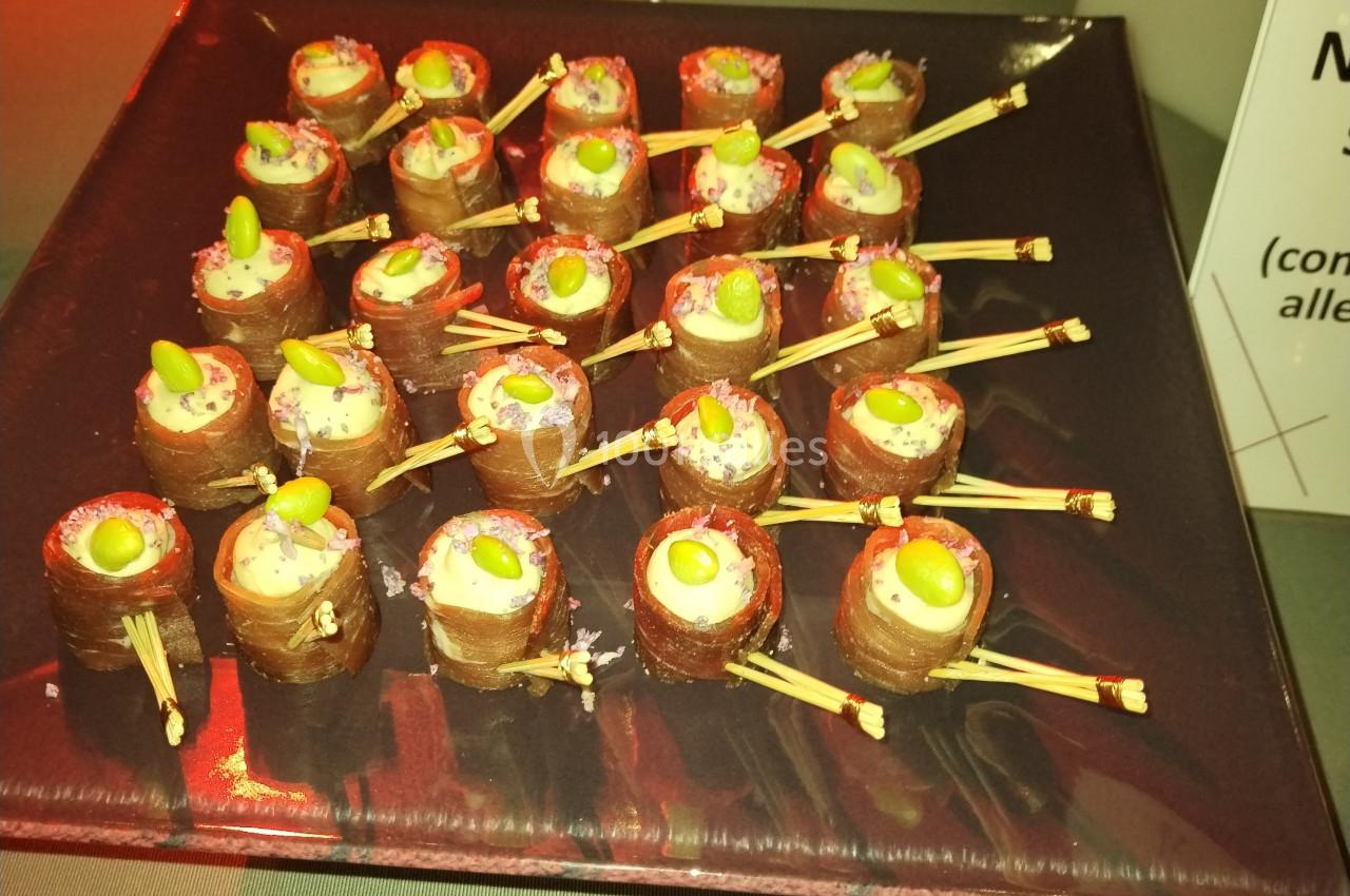 Assortiment de bouchées enroulées dans une fine tranche de viande, garnies de crème et décorées de fèves vertes.