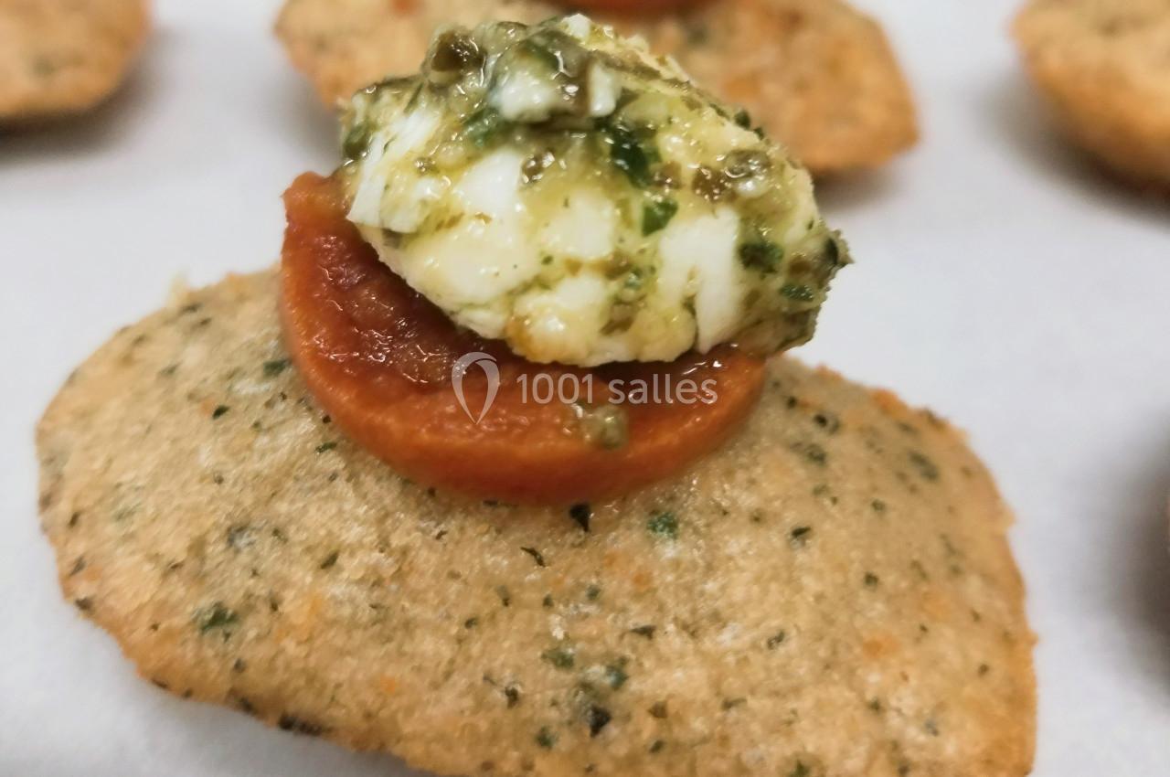 Biscuit salé garni de tomate séchée et fromage frais au pesto, présenté en gros plan.