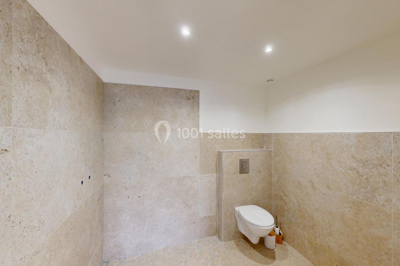 Toilettes modernes avec murs et sol en pierre beige, éclairage encastré et accessoires minimalistes.