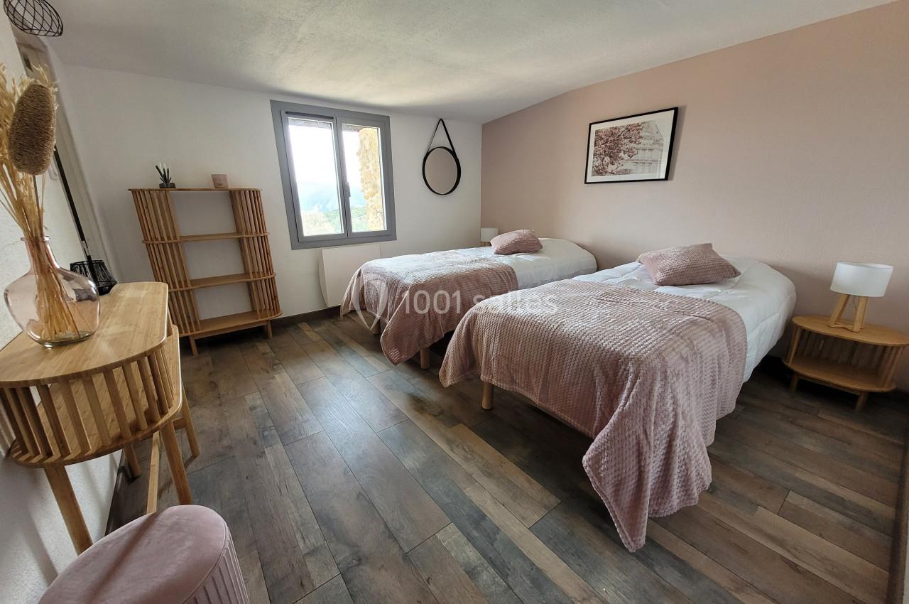 Chambre lumineuse avec deux lits simples, décoration sobre, murs clairs et mobilier en bois.
