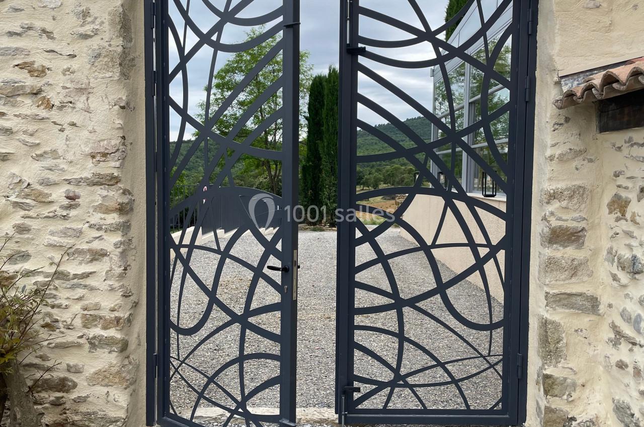 Portail métallique ajouré au design moderne, installé entre deux murs en pierre, donnant sur une allée gravillonnée.